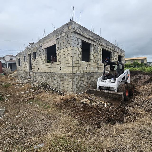 Bobcat levelling ground by a block building